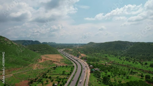 aerial drone shot flying over a winding 6 lane highway filled with vehicles surrounded by tree covered mountains with monsoon clouds overhead showing the amazing road trips in India to hill stations photo