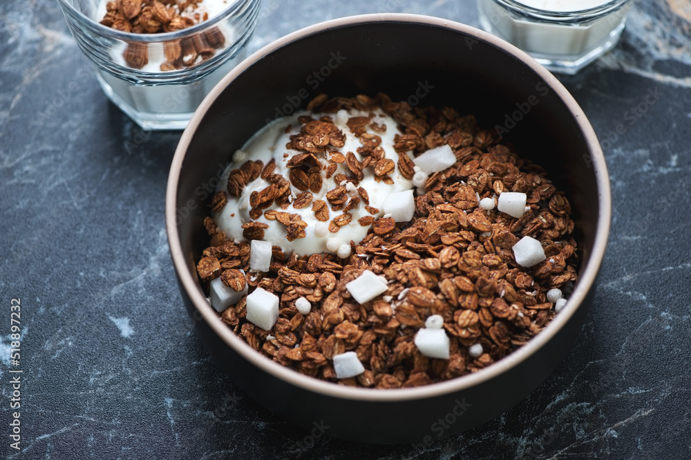 Bowl of chocolate granola with coconut and greek yogurt, middle close-up on a black marble background Bowl of chocolate granola with coconut and greek yogurt, middle close-up on a black marble background