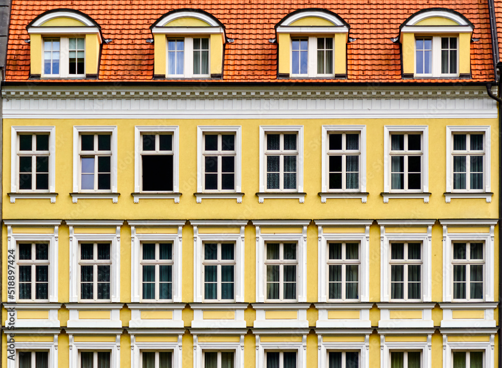 Geometrically strict yellow facade with uniformly arranged windows under a red tiled roof in Karlovy Vary, Czech Republic