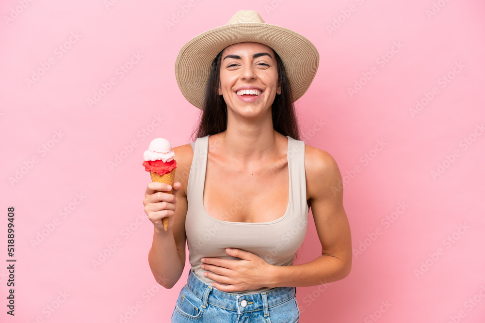Young caucasian woman with a cornet ice cream isolated on pink background smiling a lot