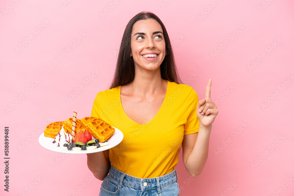 Young caucasian woman holding waffles isolated on pink background pointing up a great idea Young caucasian woman holding waffles isolated on pink background pointing up a great idea