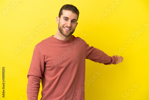 Handsome blonde man over isolated yellow background extending hands to the side for inviting to come