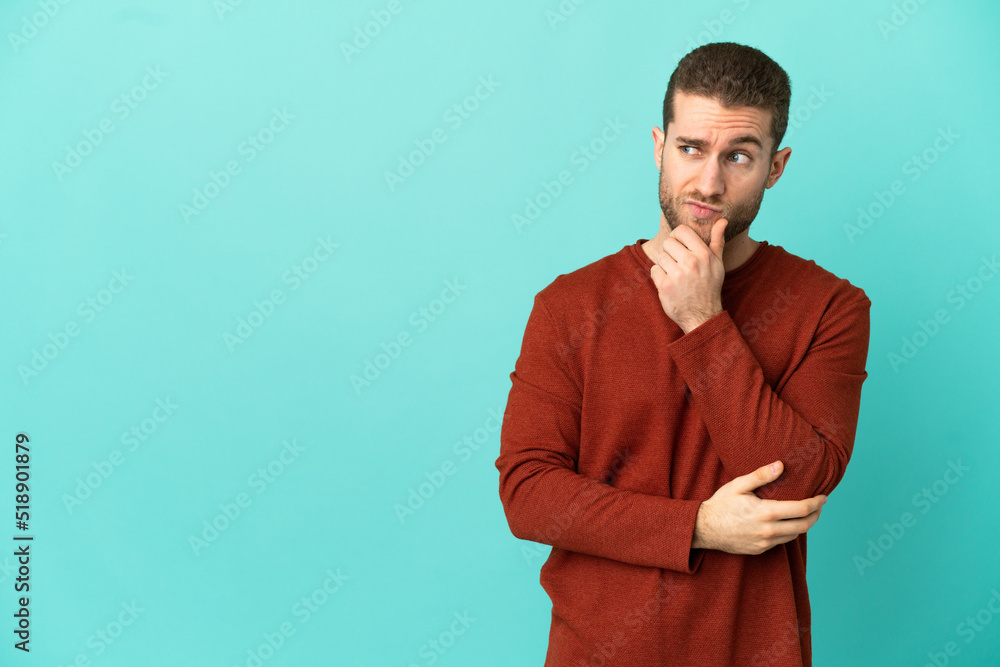 Handsome blonde man over isolated blue background having doubts and thinking