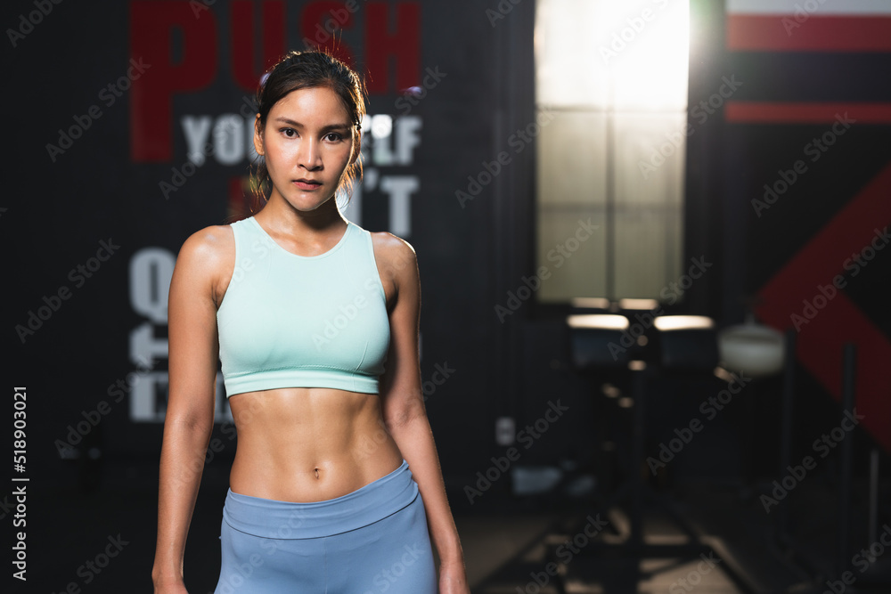 Asian athlete woman in sportswear slim muscular body posing after exercise in gym.Portrait female workout bodybuilder with sweat showing abdominal muscles at sport club fitness.