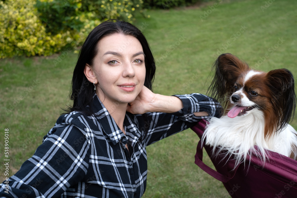 Handsome young woman take selfie with her happy papillon dog, continental toy spaniel on the backyard lawn. Woman has fun with loyal pedigree dog outdoors in summer house, park. Handsome young woman take selfie with her happy papillon dog, continental toy spaniel on the backyard lawn. Woman has fun with loyal pedigree dog outdoors in summer house, park.