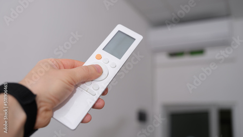 Hand with remote control is directed to air conditioner in room