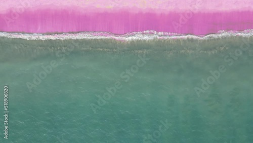 Aerial top view ocean blue waves break on pink sand beach waves crashing against an empty beach.Sea waves and beautiful pastel color