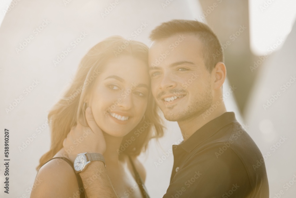 A romantic guy is holding his girlfriend in the modern urban space at the sunset in a Spain town. A couple of tourists on a date in the evening in Valencia.