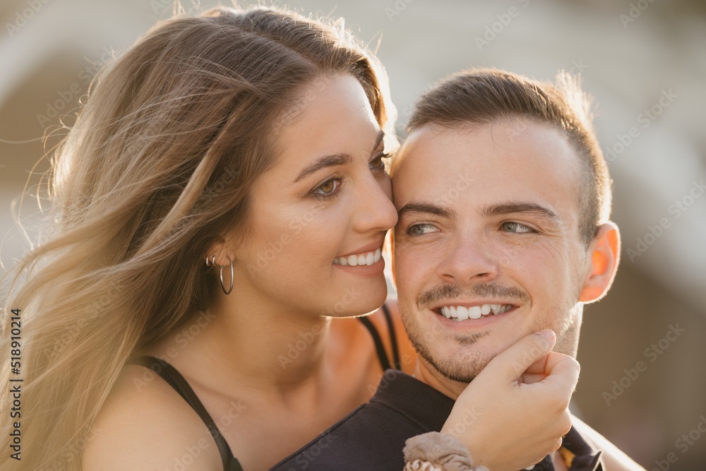 A close photo of a girl who is stroking her boyfriend from the back in the modern urban space at the sunset in Spain. A couple of tourists on a date in the evening in Valencia.