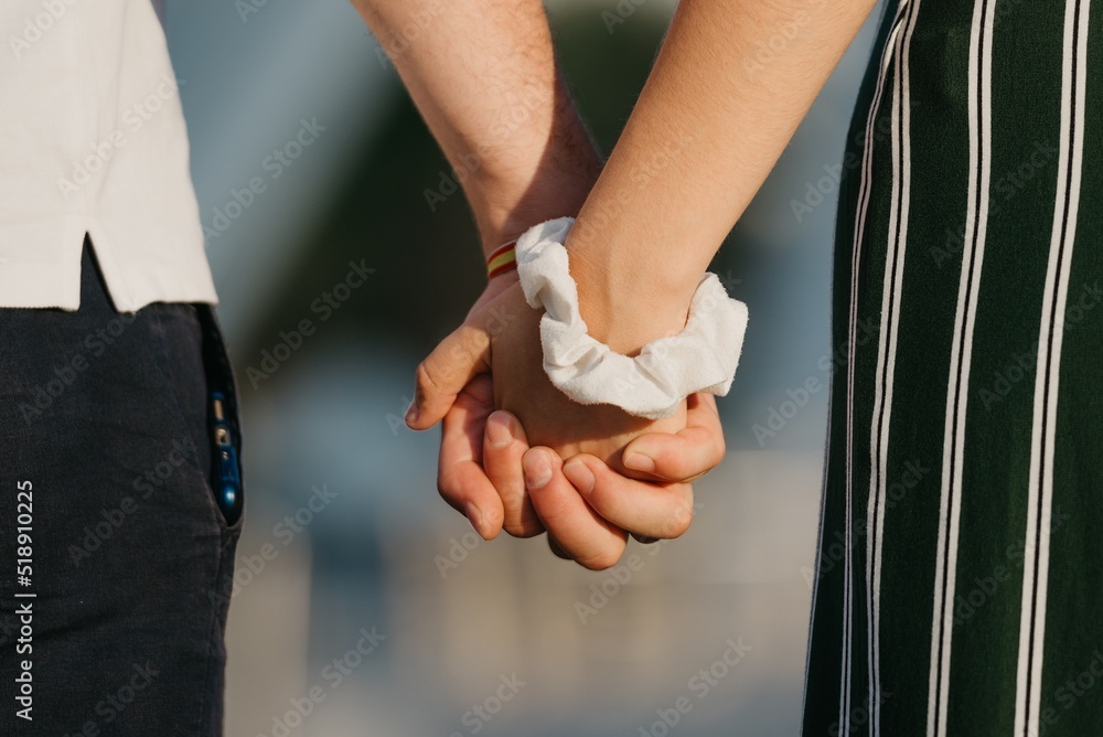 A close photo of hands which are holding each other in the modern urban space at the sunset in a Spain town. A couple of tourists on a date in the evening in Valencia.