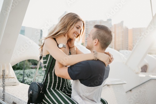 Obraz na płótnie A close photo of a smiling girl who is hugging her boyfriend in the modern urban space at sunset in Spain. A couple of tourists on a date in the evening in Valencia. w salonie