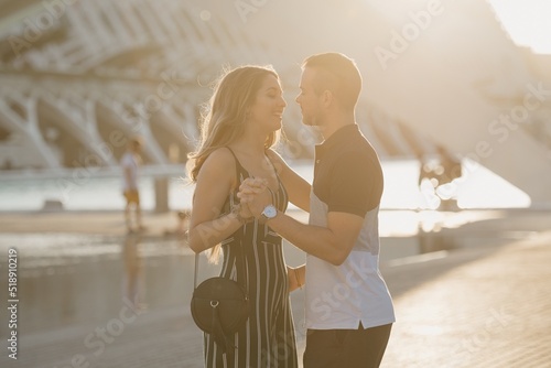 Obraz na płótnie A couple of tourists is dancing in the modern urban space on a date at the sunset in Valencia. A smiling girl is holding hands with her romantic boyfriend in the evening in Spain. w salonie
