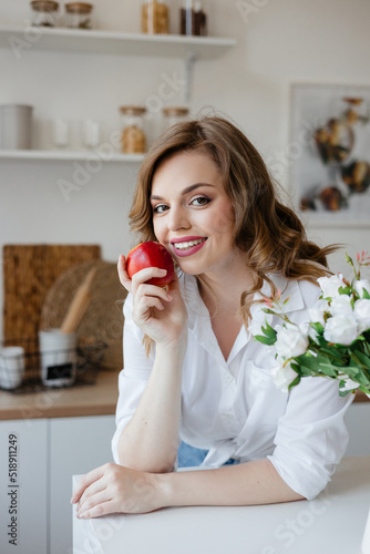 Beautiful girl eating a red apple in the kitchen