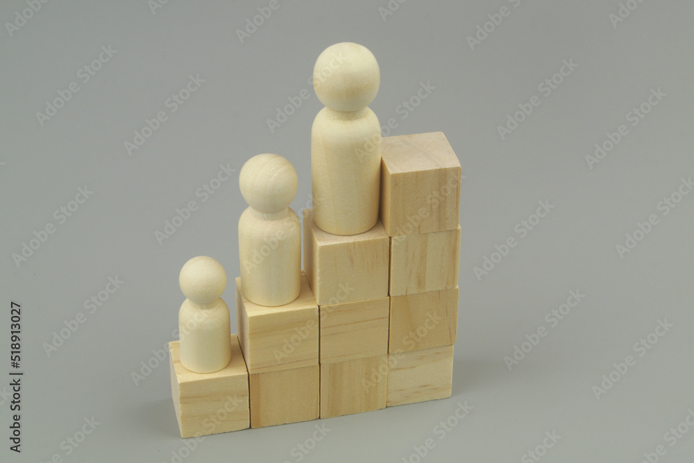 Wooden people figures with different size as employers on stair made of cubes on gray background. Wooden people figures with different size as employers on stair made of cubes on gray background.