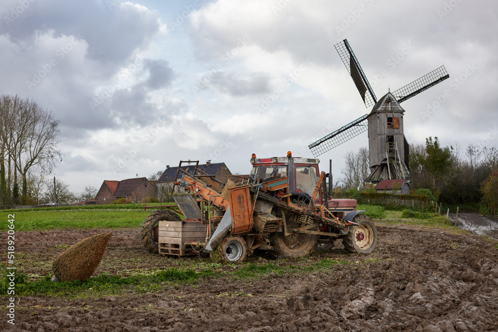 Fototapeta premium Old tractor on field with windmill in background