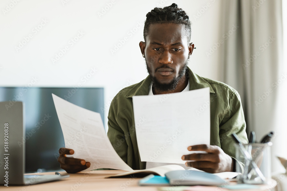 Remote career, freelance job concept. Focused black man working at home and looking through business documents Remote career, freelance job concept. Focused black man working at home and looking through business documents