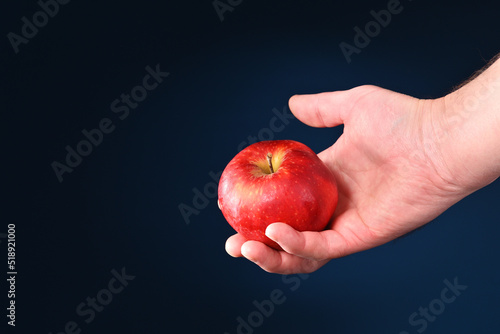 Red apple in man's hand on a dark background.