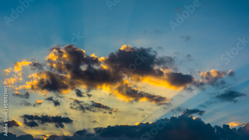 Sun rays and sunlit clouds in blue sky at sunset