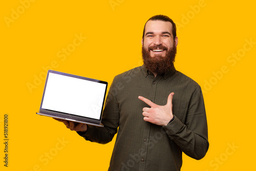 A photo of a bearded man and his computer and him pointing at it while smiling