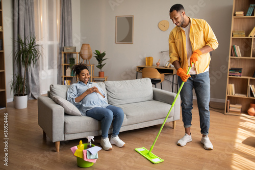 Black Husband Doing House Chores While Pregnant Wife Resting Indoor