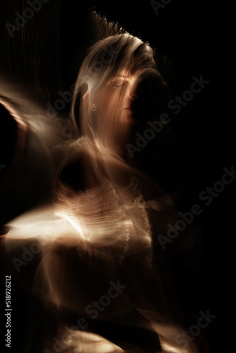 Abstract woman silhouette in light trails of light painting with golden light beams. Portrait in the style of light painting. Long exposure photo. Image contains noise and motion blur