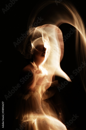 Abstract woman silhouette in light trails of light painting with golden light beams. Portrait in the style of light painting. Long exposure photo. Image contains noise and motion blur
