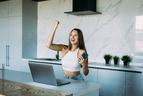 Young woman use phone with win gesture in the kitchen