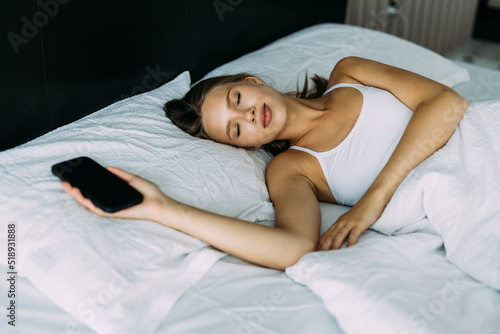 Young Woman sleeping in bed and holding a mobile phone.