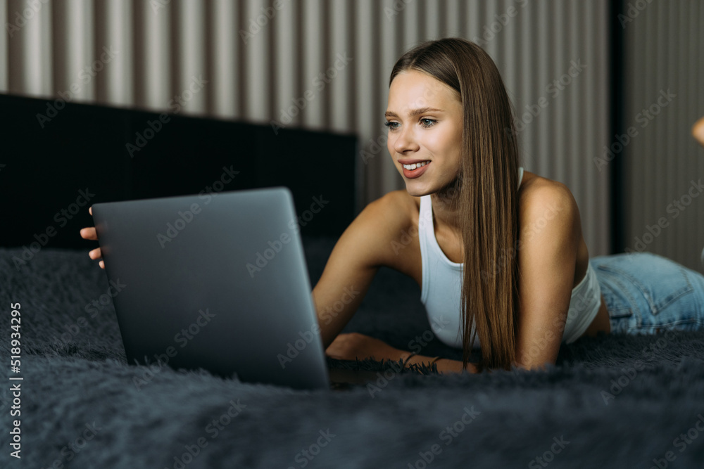Smiling woman catching up on her social media relaxes in bed with a laptop computer on a lazy day Smiling woman catching up on her social media relaxes in bed with a laptop computer on a lazy day