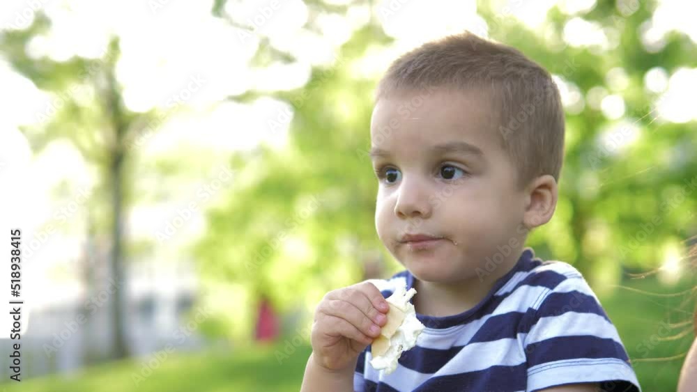 Close-up of a little boy sitting in a park on a lawn on a bright sunny summer day and eating an ice cream waffle. Happy childhood in the fresh air. Family in the park at sunset Close-up of a little boy sitting in a park on a lawn on a bright sunny summer day and eating an ice cream waffle. Happy childhood in the fresh air. Family in the park at sunset