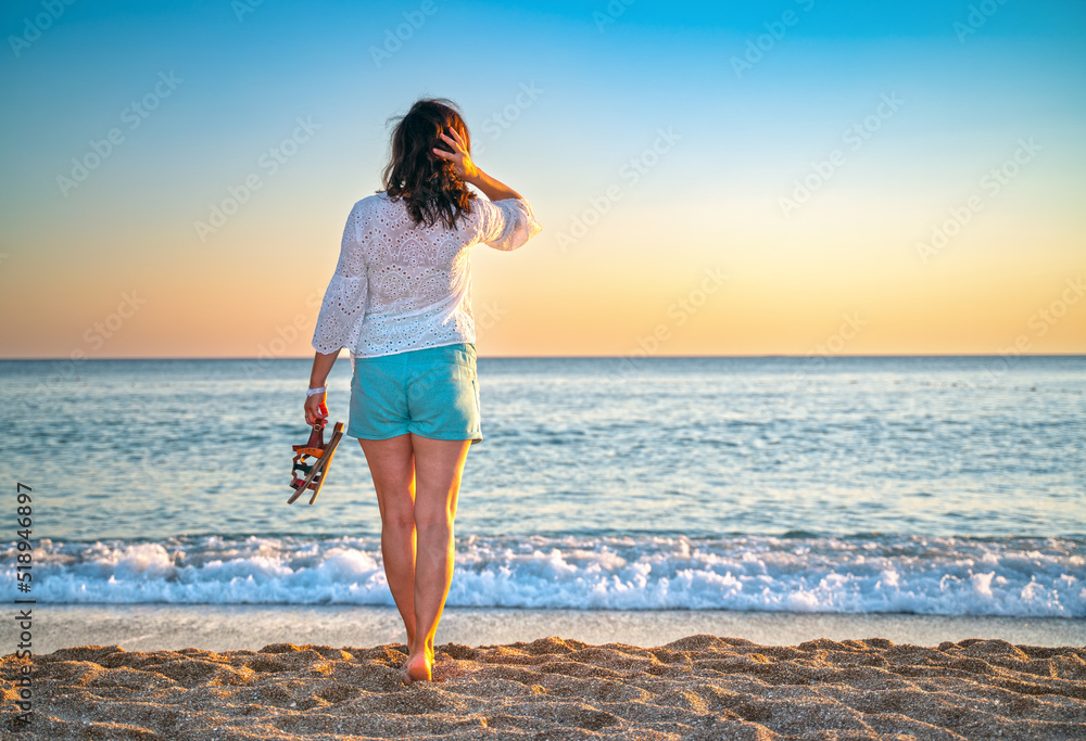 Happy Carefree Woman Enjoying Beautiful Sunset on the Beach with sandals in hand.