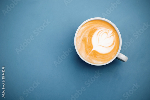 Cup of cappuccino with a flower on a blue surface