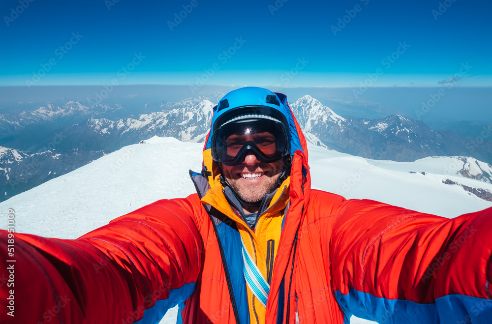 Selfie shot of a happy smiling at camera man dressed red warm mountaineering down jacket on Kazbek (Kazbegi) summit 5054m while he successfully achieved the summit. East Caucasus mountains, Georgia. Selfie shot of a happy smiling at camera man dressed red warm mountaineering down jacket on Kazbek (Kazbegi) summit 5054m while he successfully achieved the summit. East Caucasus mountains, Georgia.