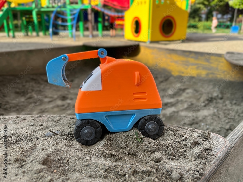 Closeup of the orange toy excavator with a blue grab bucket and black wheels in the sandbox on a playground