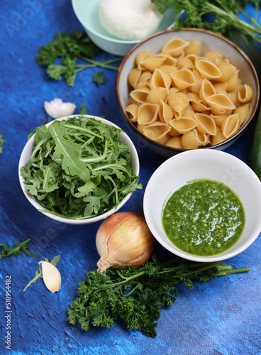 Pasta pesto ingredients on a table. Close up photo of pasta, mozzarella, zucchini, parsley, garlic, onion and pesto sauce. Balanced menu concept. 