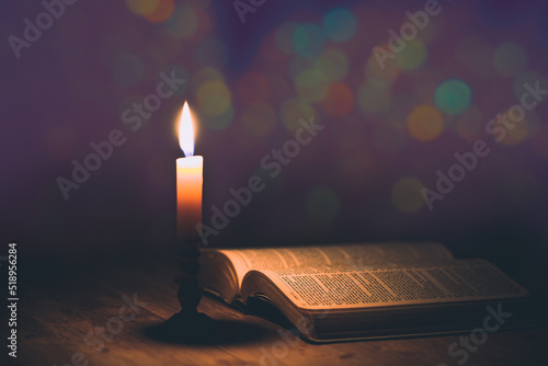 Candle with bible on a old oak wooden table.