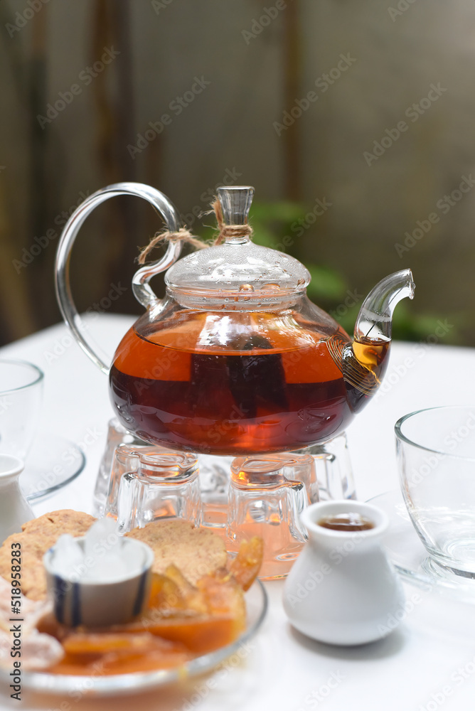 Earl Grey tea in glass teapot with cups and crystalized fruits on wooden background Earl Grey tea in glass teapot with cups and crystalized fruits on wooden background