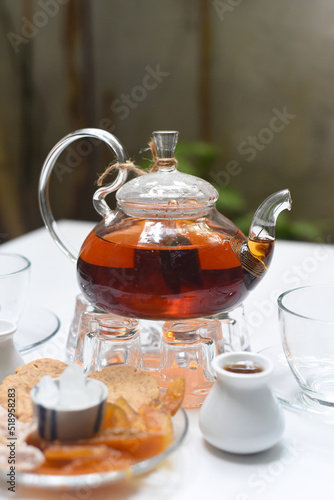  Earl Grey tea in glass teapot with cups and crystalized fruits on wooden background