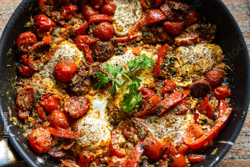Shakshuka - fried eggs with sausages and vegetables in frying pan 