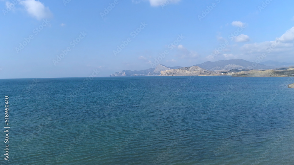Aerial for a sandy beach, deep blue water of the Mediterranean sea with small waves. Shot. Seascape with mountains on the horizon and on blue sky background.
