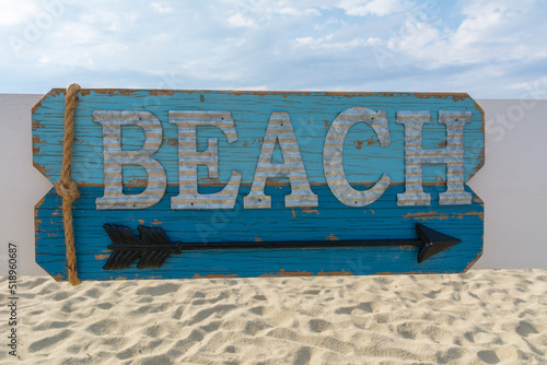 Wooden beach sign on background with sand and blue sky