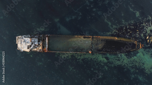 Aerial top view for wrecked ship along the rocky coast in blue water. Shot. Old sunk boat near sea shore, view from above.