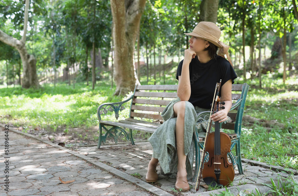 Woman wearing woven hat sitting on old and rust chair,holding violin and bow in hand,