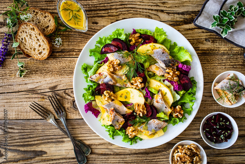 Marinated herrings with roasted beetroots, apple, walnuts  and fresh vegetable leaves on wooden table
