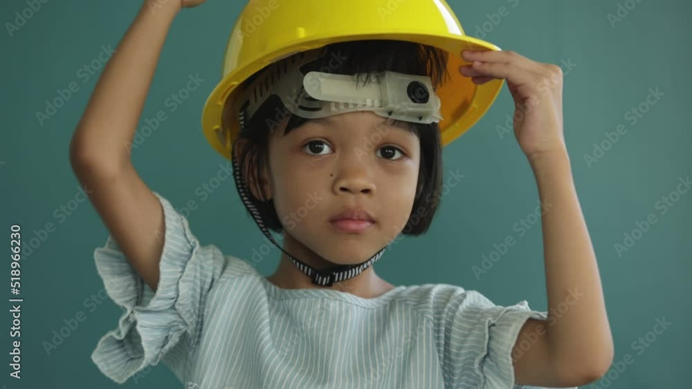 Portrait Thai Asian kid girl, aged 4 to 6 years old, cute and healthy, she is learning and practicing to wear a yellow helmet. to prevent things from falling on the head and shockproof Portrait Thai Asian kid girl, aged 4 to 6 years old, cute and healthy, she is learning and practicing to wear a yellow helmet. to prevent things from falling on the head and shockproof