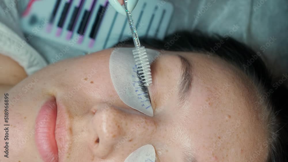 eyelash extension master combs the extended eyelashes on the eye of a beautiful woman with a brush eyelash extension master combs the extended eyelashes on the eye of a beautiful woman with a brush