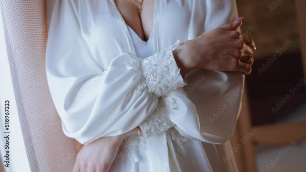 A sexy beautiful girl stands by the window in underwear and a satin robe with beaded cuffs on the sleeves. A woman hugs herself with her arms. Luscious breasts. Morning of the bride A sexy beautiful girl stands by the window in underwear and a satin robe with beaded cuffs on the sleeves. A woman hugs herself with her arms. Luscious breasts. Morning of the bride