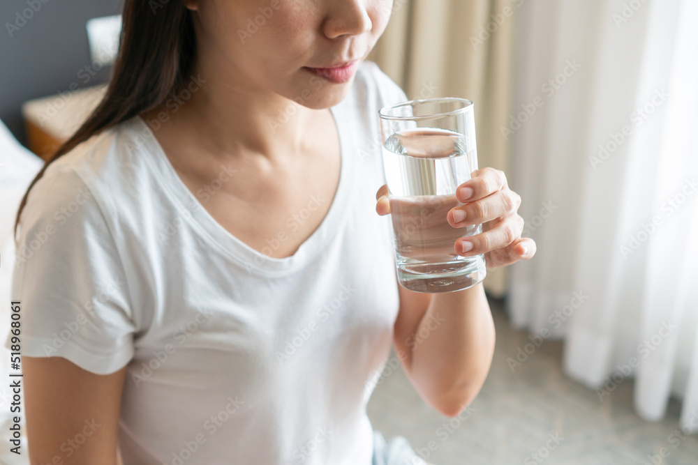 Healthy young Asian woman smiling and enjoying fresh clean water while sitting on bed in morning. Diet girl drinking water after wake up. Concept of health and freshness, thirst, water purification Healthy young Asian woman smiling and enjoying fresh clean water while sitting on bed in morning. Diet girl drinking water after wake up. Concept of health and freshness, thirst, water purification