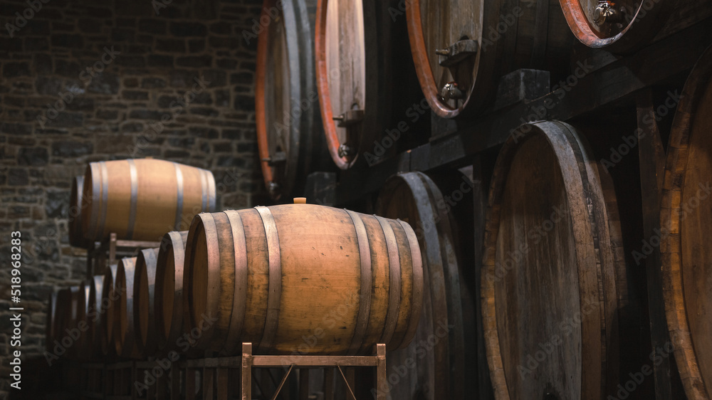 The ambiance of the traditional wine cellar, aging red wine barrels, wooden casks in rows in the winery underground storage room The ambiance of the traditional wine cellar, aging red wine barrels, wooden casks in rows in the winery underground storage room