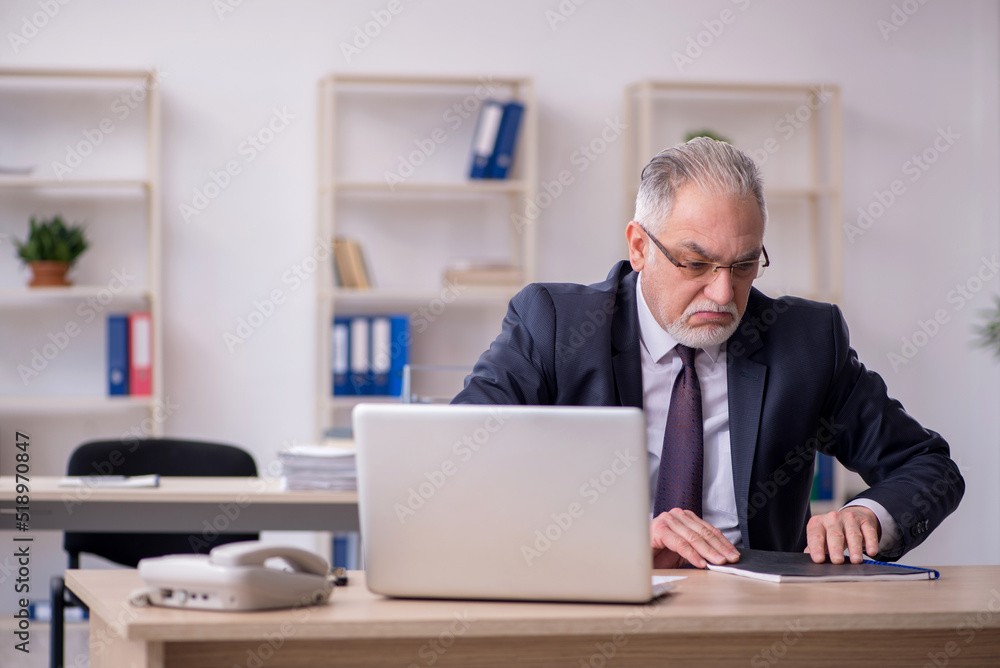 Old male employee sitting at workplace Old male employee sitting at workplace